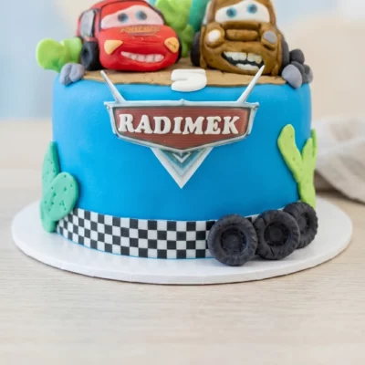Detail dortu Auta se šachovnicovým pruhem, pneumatikami, kaktusy a jmenovkou ve stylu závodního znaku.