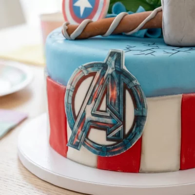 Detail boku dortu Avengers s plochým logem, červenobílým zdobením a částí modelovaného kladiva na horní straně.