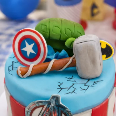 Detail dortu Avengers s modelovaným štítem, kladivem, zelenou pěstí a kreslenými prasklinami na modrém povrchu.