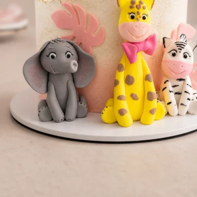 Detail čelních modelovaných zvířátek na safari dortu se slonem, žirafou, zebrou a růžovými listy.