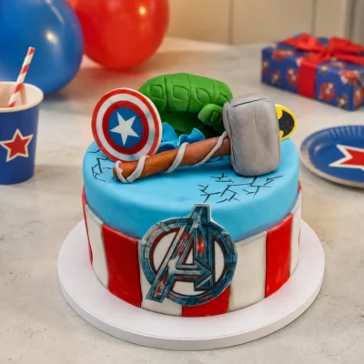 Superhrdinský dort Avengers se světle modrým vrškem, červenobílým bokem, modelovaným štítem, kladivem a zelenou pěstí.