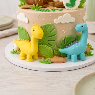 Detail spodní části dinosauřího dortu se dvěma modelovanými dinosaury, zelenými listy, obláčky a přírodními detaily.