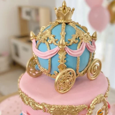 Detail modro-růžového kočáru se zlatým zdobením na horním patře princeznovského dortu.