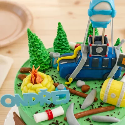 Horní detail dortu Fortnite s Battle Busem, táborákem, truhlou, stromky a akčními herními dekoracemi.