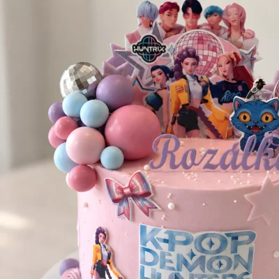 Detail růžového dortu s kaskádou pastelových koulí, disco koulí a barevnou mašlí.