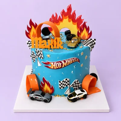 Modrý dort Hot Wheels s autíčky, oranžovými oblouky dráhy, velkými plameny a šachovnicovými vlajkami.