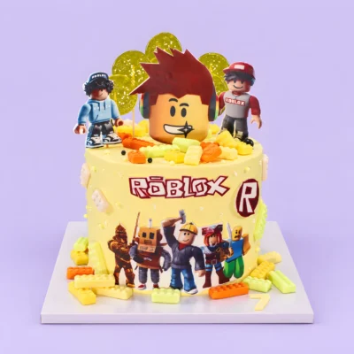 Žlutý dort Roblox s velkou hlavou ve sluchátkách, postavami v kšiltovkách, obrázky avatarů vpředu a kostičkami na podložce.