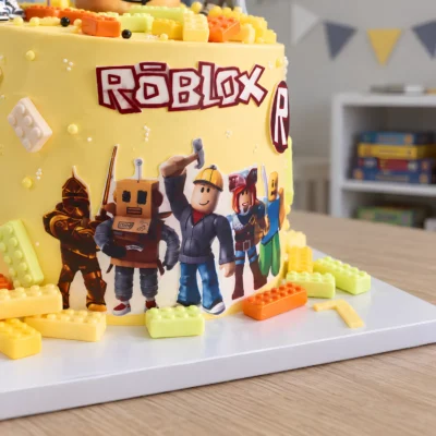 Detail plochého motivu postav Roblox na žlutém boku dortu s barevnými kostičkami na podložce.