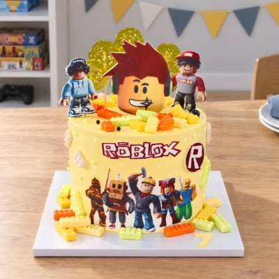 Celý žlutý dort Roblox z čelního nadhledu s horními dekoracemi a kostičkami na čtvercové podložce.